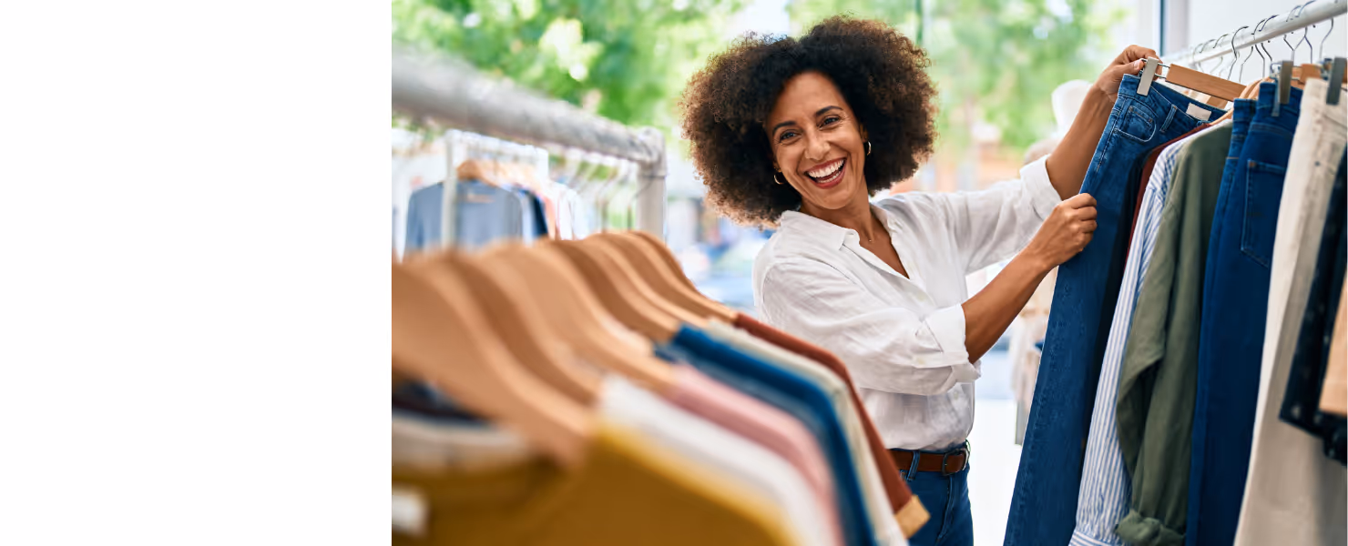 Lachende vrouw tussen kledingrekken met kleding.