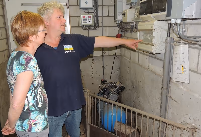 Varkenshouder en zijn vrouw, wijst naar meterkast in de stal.